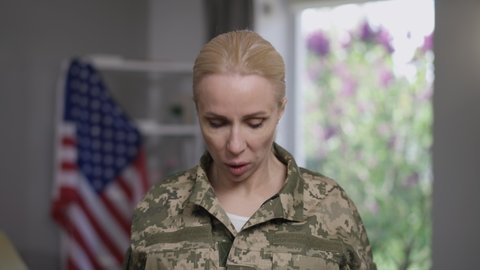 Close-up portrait of anxious military woman with PTSD unzipping camouflage uniform breathing rapidly. Young beautiful stressed worried female soldier with symptoms of psychiatric disorder indoors