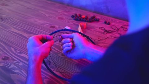 Artisan makes dreamcatcher in art studio. Master in dark workshop with neon red and blue lighting.