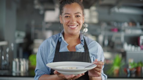 Restaurant Kitchen: Portrait of Black Female Chef Prepares Dish, Tasting Food, Enjoying it. Professional Cook Eats Delicious, Authentic, traditional Food using only Healthy Ingredients for Meal Recipe