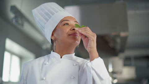 Black Female Chef Takes Fresh Herb, Enjoys Smell with a Smile, Secret Ingredient that Makes Grandmother's Recipe Special. Traditional Restaurant Kitchen with Authentic Dish, Healthy, Nurturing Food