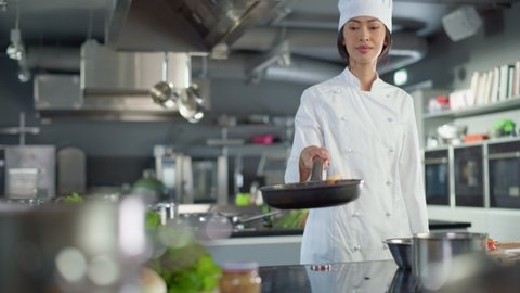 Restaurant Kitchen: Portrait of Asian Female Chef Holds Frying Pan with Flame, Stirs Her Favourite Flavourful Dish, Smiles. Professional Cook Delicious and Traditional Authentic Food, Healthy Dishes