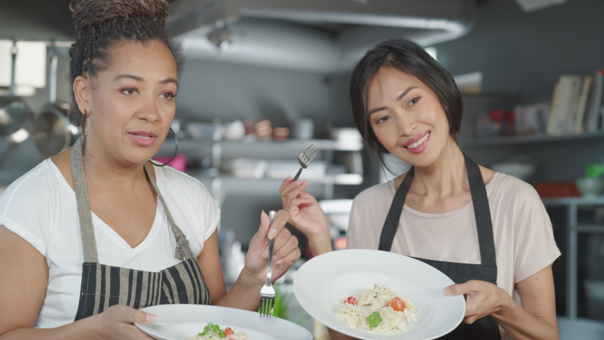 TV Cooking Show Kitchen with Two Master Chefs. Asian and Black Female Presenters Talk, Show Dish at Camera Taste Deliciously Cooked Food and Enjoy it, Celebrate with High-Five. Online Video Class