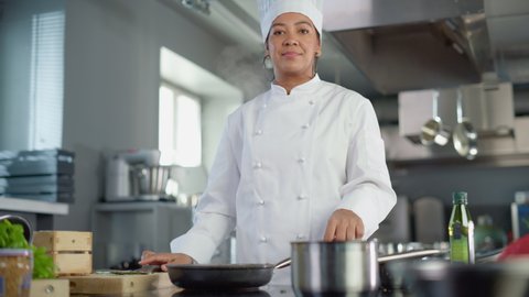 Restaurant Kitchen Cooking: Portrait of Black Female Chef Ads Oil, Holds Frying Pan, Stirs Her Favourite Flavourful Dish, Smiles. Professional Cook Delicious, Traditional Authentic Food, Healthy Dish