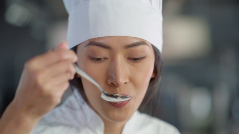 Restaurant Kitchen: Portrait of Asian Female Chef Preparing Dish, Tasting Food and Enjoying it. Professional Cooking Delicious, Authentic, traditional Food, using Healthy Ingredients for Meal Recipe