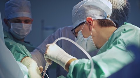 Male surgeon in glasses leading the operation. Group of surgeons use operational instruments and devices for trauma operation.