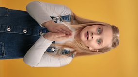 VERTICAL VIDEO POV surprised girl shocked amazement positive emotion covering mouth by hands. Adorable female kid excited astonishment sudden unexpected expression posing isolated on orange studio