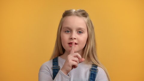 Closeup portrait playful female kid shhh gesture silence quiet with forefinger near lips posing isolated on orange studio. Cute baby girl mystery secret noise mute shh gesturing with positive emotion 