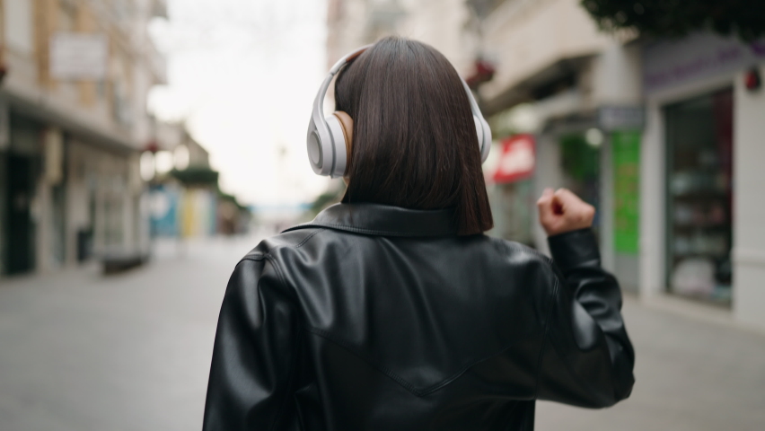Young hispanic woman on back view listening to music at street