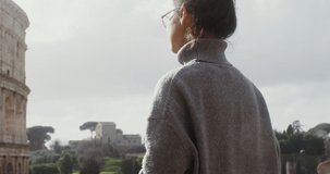 A young woman of European appearance in glasses, dressed in a warm sweater, photographs the Colosseum on a mobile phone, close-up. Italy Rome. Video in 4k, red komodo.