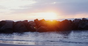 A young beautiful warmly dressed woman of European appearance walks along the seashore at sunset in the red light of the sun, looking into the distance at the sea. Video in 4k, red komodo.