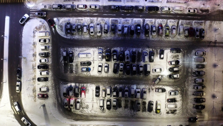 Car parking lot free of charge aerial view at night. Overhead aerial of a car trying to find a parking spot in a busy parking lot. Aerial top view of many cars parked.	