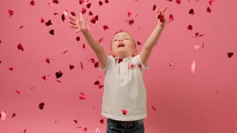 Slow Motion Video Boy Celebrates Valentines Day in Confetti of Hearts. Blond Boy Throws up Red Confetti in Shape of Hearts, Smiles and Tries to Catch Heart With his Hands on Yellow Background.