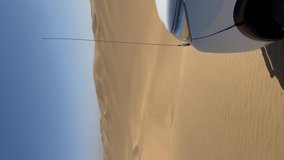 Vertical video. White off-road SUV car parked at Sandwich Harbour in Namibia at coast of Atlantic Ocean. Sandy beach, dunes on seashore. Summer vacations, wild desert nature in Africa. Namib-Naukluft.