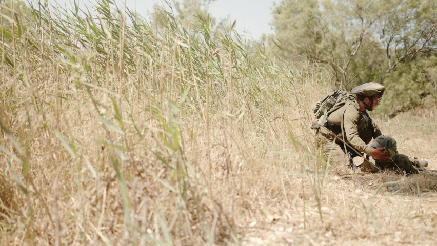 Male soldier looking around while supporting the head of his teammate until he is seeing a waterpool. Steady shot