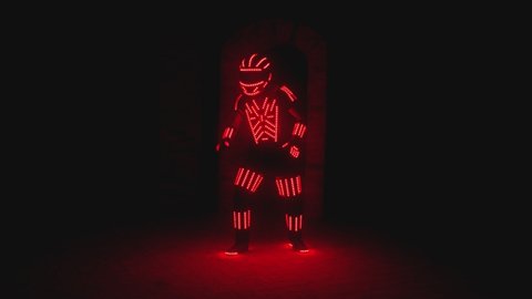 Man dressed in led illuminated costume with colorful lights dancing and moving inside dark interior or club . Dancer guy wearing clothing with neon lights on his body and dances . Shot on ARRI camera