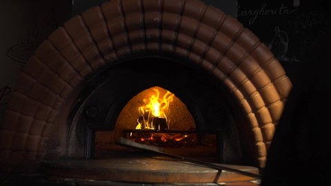Pizzaiolo is putting pizza in the wood-fired oven. The pizza is cooking in the oven. The salami pizza is going into the oven. Chef putting pizza with a shovel into the wood-fired oven. Slow motion