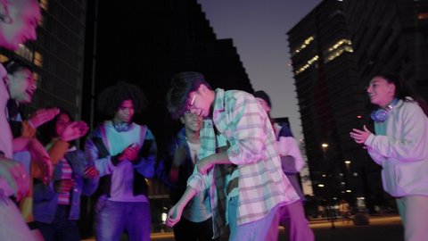 Multiracial Group of freestyle dancers performing different moves on the dark street.