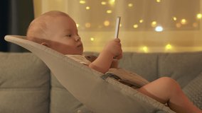 Cute kid holding remote control for TV digital media player and watching TV. Baby boy watches cartoons sitting in rocking chair. High quality 4k footage