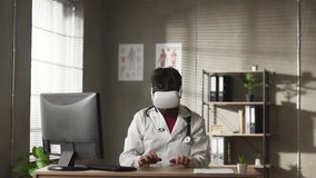 Portrait of professional Caucasian male doctor in VR glasses sitting in hospital cabinet and typing using virtual reality innovations - Powered by Shutterstock - Get 15% off with code: PIKWIZARD15