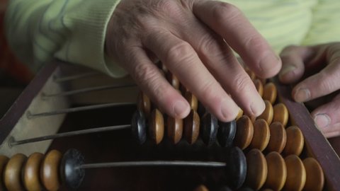 Close view of senior man wrinkled hands counts with retro abacus beads. Home finance and money saving conception.