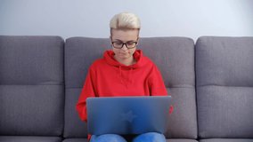 Young woman working on laptop at home. Professional freelancer person sitting on couch at home and doing distant work on notebook computer. Focused female with short tom boy haircut studying online
