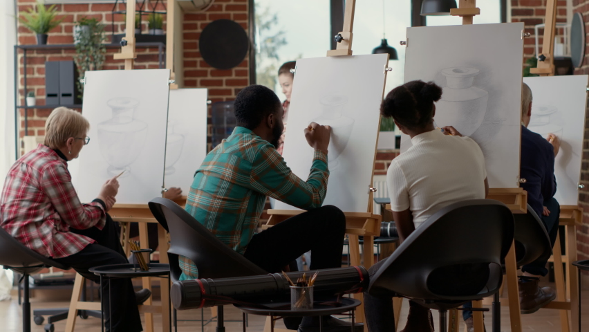 Young students drawing on canvas and talking about artwork in artistic workshop, doing sketch practice to learn new creative skills. Attending ducational class to draw vase. Tripod shot.