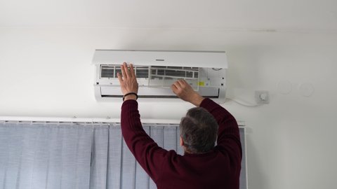 Back view of one senior caucasian man cleaning repairing air-condition at home changing filter taking out removing or putting back