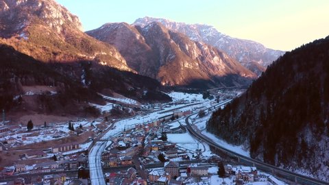 Beautiful aerial perspective of Pontebba city situated in Udine, Italy. Drone pan left creating a beautiful panorama of the city. Sunrise with warm colours. In background Italian Alps mountain.
