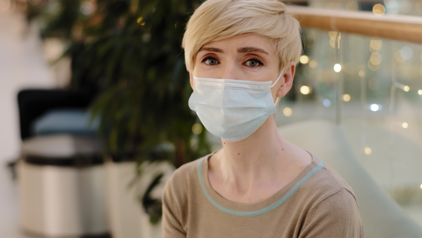 Portrait caucasian middle aged mature 40s 45s woman lady with short haircut wears medical protective mask sitting indoors in mall in looking at camera coronavirus pandemic contagious infection virus