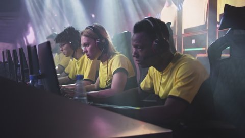 Young female gamer esportsman player with blond hair taking off headset and clasping hands with black teammate after victory in video game match during professional esports tournament