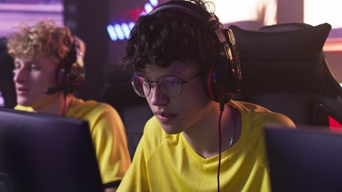 Anxious teenager esportsman game player in glasses playing video game then shaking hands of teammates and celebrating victory during professional tournament