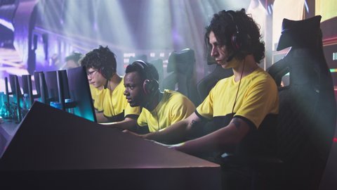 Angry esportsman gamer player breaking keyboard and touching head while expressing disappointment sitting near teammates after loss in professional video game match