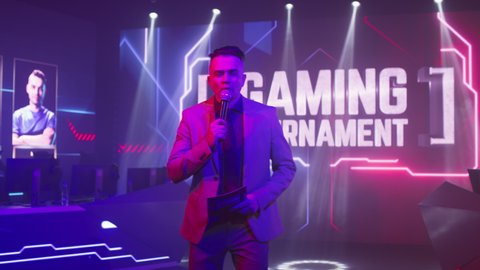 Adult man host gesticulating and looking at camera while standing under neon illumination and announcing professional gaming tournament