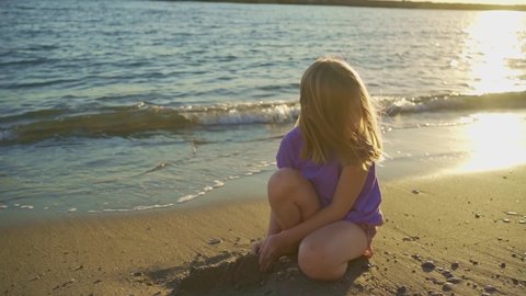 a cute little girl sits on the seashore, playing in the sand and with pebbles. sand castles. children's games on the beach. travelling with children. travel agencies and vouchers.