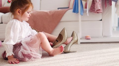 cute little girl putting the high heel shoes on, sunny room at home