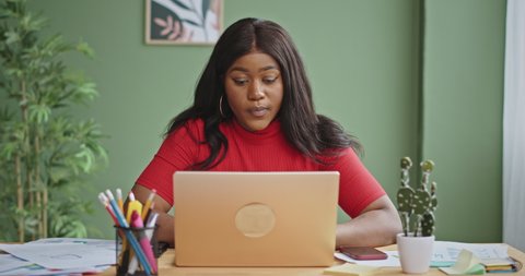 Shocked African American manager working in office. Worried black businesswoman touching and shaking head after reading shocking data on laptop while sitting at table during work on business project