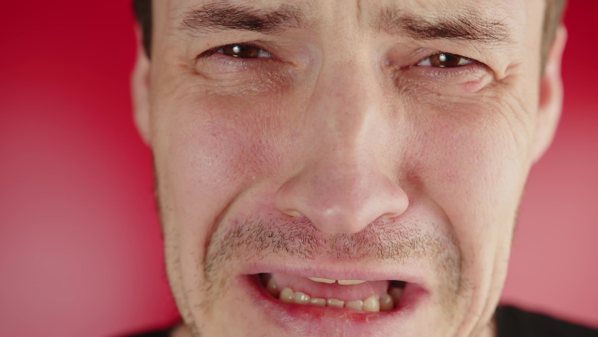 Portrait of a crying man on a red background. An unshaven man is crying and grieving