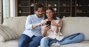 Young 30s couple sit on couch read great news on smart phone, got unbelievable commercial offer, rejoicing long awaited sale gesturing feel overjoyed, exulting after winning on-line lottery concept