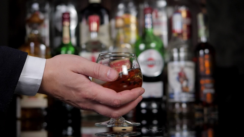 Close-up of a businessman in a shirt and jacket holding a glass of cognac in a bar. A man relaxes after a hard day's work.