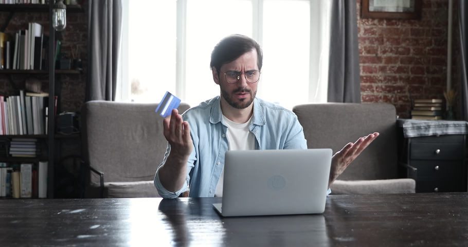 Angry millennial male in glasses hold prepaid card look on pc screen feel mad annoyed get payment rejection after entering wrong password. Worried young man overspend money on electronic bank account Royalty-Free Stock Footage #1086169439