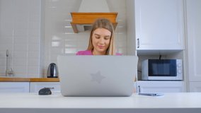 Focused young woman working on laptop at home. Beautiful white female doing distant work on notebook computer during lockdown. Cheerful Caucasian person studying online in 4k stock footage