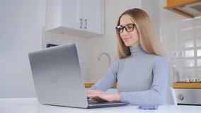 Beautiful white woman working on laptop computer at home on lockdown. Attractive young adult female with long blonde hair typing text on notebook pc in 4k video. Freelancer person doing distant work