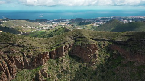 Stunning areal view over the edge of a volcano crater in Gran Canaria against the backdrop of lush green valleys, small villages of Canary islands and the Atlantic ocean in the background.