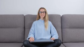 Happy white woman start working on laptop computer on couch at home during lockdown. Cheerful freelancer female looking in camera and then opens notebook pc and starts doing distant work online