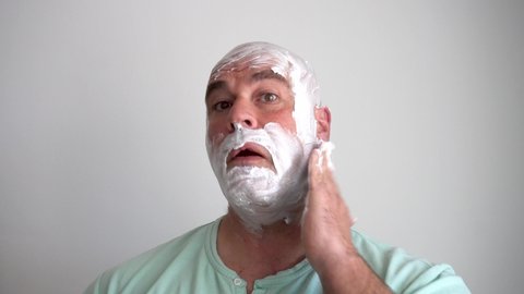 Close up of Caucasian man spreading shaving cream on his face and head to shave