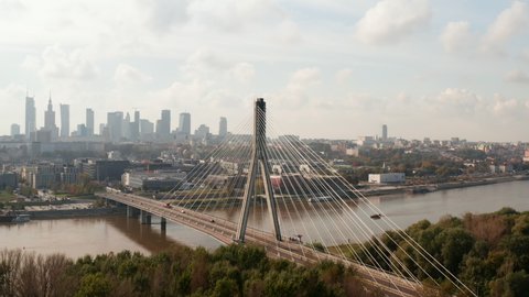 Slide and pan shot of beautiful modern design bridge spanning river. Skyline with downtown high rise office buildings in background. Warsaw, Poland