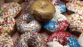 4K HD video panning across Vanilla and Chocolate frosted donuts with candy sprinkles on display for sale. High sugar fast food treat
