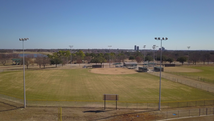 4K aerial of an empty baseball field on a sunny day. Inspirational sports view of youth athletics at a public park.  View from the outfield near massive lights. Royalty-Free Stock Footage #1086196109
