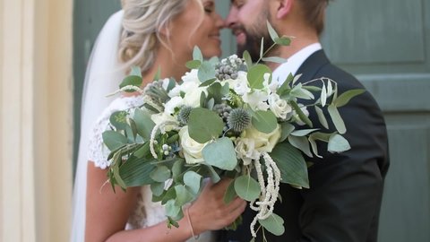 Happy wedding couple that are eskimo kissing with wedding bouquet. Young caucasian bride and groom. Man and woman in love. Newlyweds. Bride in wedding dress. Bride Groom in jacket. Slow motion.