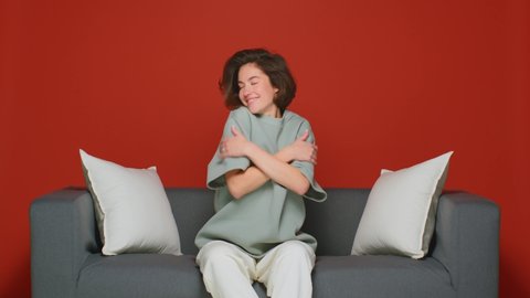 Cute positive young girl hugs herself. Pats on the shoulders. Narcissism or the cozy comfort of home. Isolated on a red background.